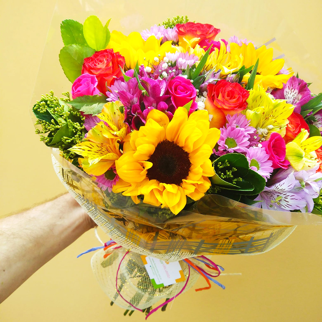 Buquê multicolorido com margaridas lilases, alstroemérias coloridas, girassóis, e rosas laranjas e pink